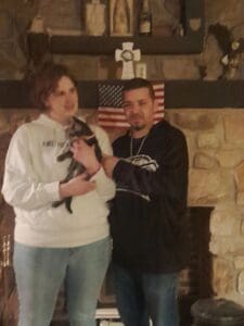 A man and woman holding a cat in front of an american flag.