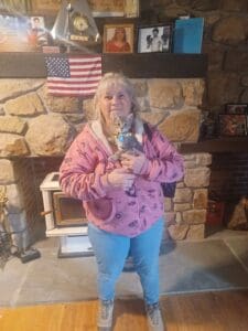 A woman holding her cat in front of the fireplace.